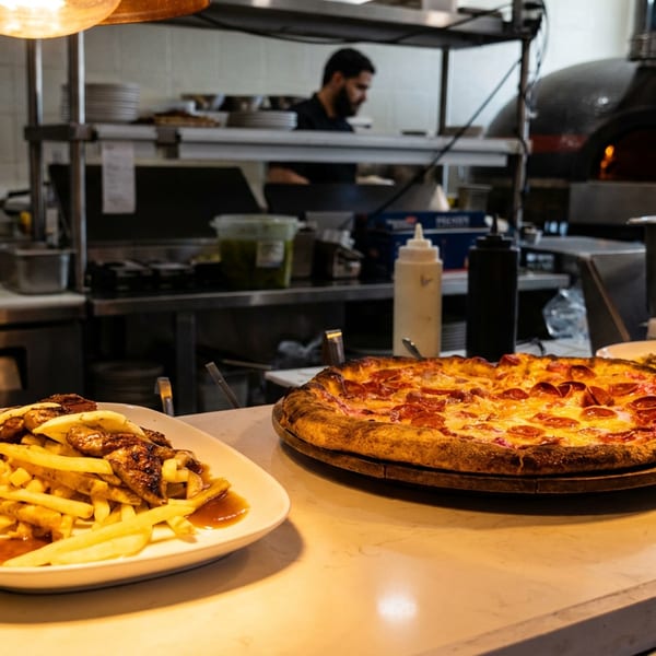 Pepperoni pizza, fries, and another dish on a counter in a restaurant kitchen with a chef.