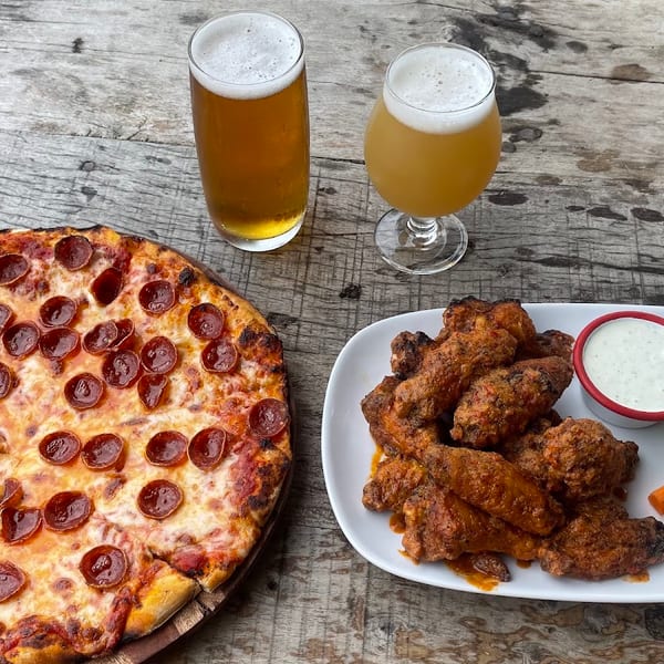 Pepperoni pizza, buffalo wings with ranch, celery, carrots, and two beers on a wooden table.